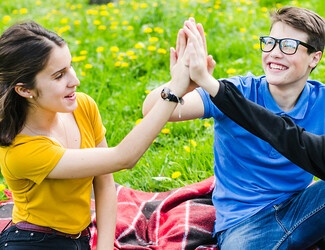 Young adults high-fiving each other outside on a picnic blanket